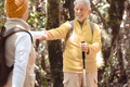 Cheerful caucasian senior couple hiking in the forest holding backpacks and walking sticks - PhotoDune Item for Sale
