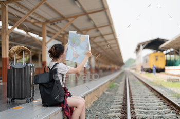 Young asian woman using generic local map, siting alone at train station platform with luggage