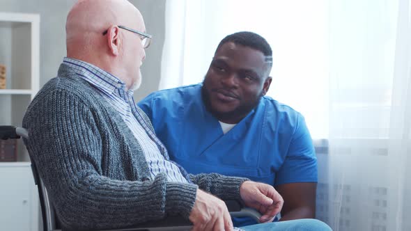 African-American caregiver and old disabled man in a wheelchair. Nurse and handicapped patient.