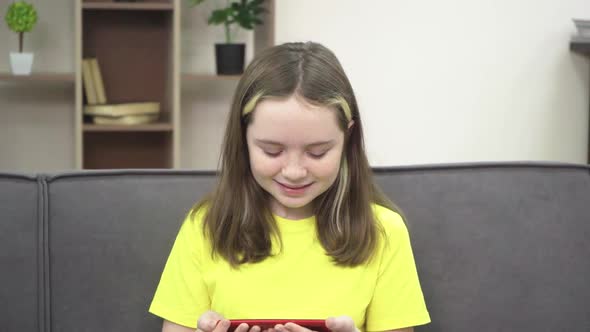 The Little Girl is Smiling and Looking at Her Phone While Sitting on the Couch