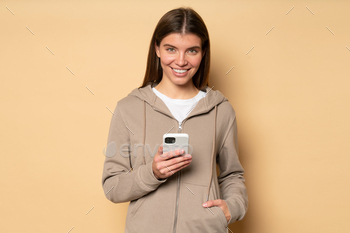 in morning or jogging in park, wearing sport hoodie, looking at camera with happy smile holding hand in pocket on brown background