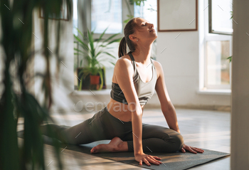 Young fit woman practice yoga doing asana in light yoga studio with green house plant