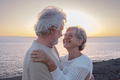 Portrait of happy and romantic senior couple embraced at sea at sunset light looking into the eyes - PhotoDune Item for Sale