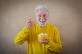 Happy white-haired senior man in yellow isolated on a light background holding a bowl of cut melon - PhotoDune Item for Sale