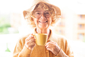 Portrait of happy beautiful curly senior woman in yellow with hat holding a coffee cup - PhotoDune Item for Sale