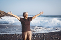 Happy mature senior woman with outstretched arms standing on the beach at sunset looking away - PhotoDune Item for Sale