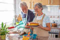 Elderly woman in home kitchen displays to her husband a baked homemade plumcake served with berries. - PhotoDune Item for Sale