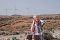 Alternative energy, wind farm. Senior woman sitting in wind turbines countryside while using phone - PhotoDune Item for Sale