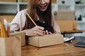 Happy young start up small business owner packing writing address on cardboard box. freelance woman - PhotoDune Item for Sale