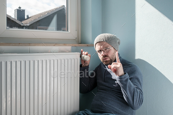 r the radiator and turns the thermostat to the minimum, making a warning gesture. Concept of crisis and increase in fuel costs.