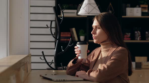 Young woman sitting by the window at the bar counter in coffee shop.