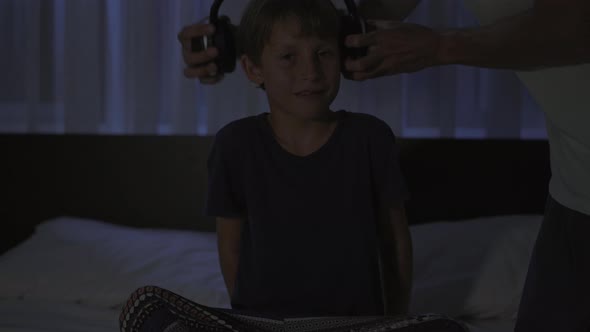 A Man at Night Turns on a Meditation Relaxation Application on His Phone for His Son to Relax Before