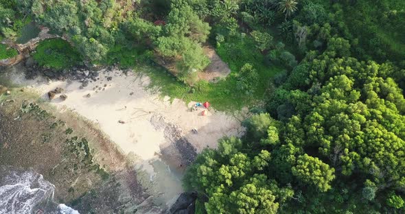 Aerial top down shot of small sandy beach with sea and forest trees in background. Someone set up te