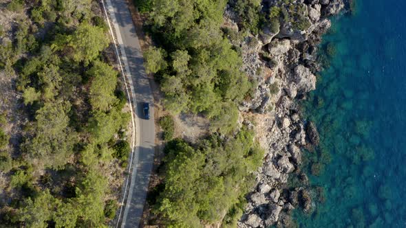 Drone track car driving on coastal highway by azure blue water; top down