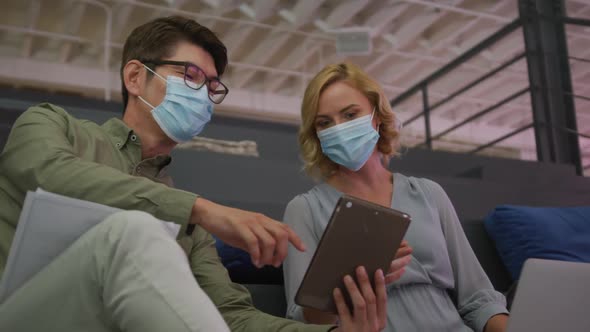 Asian man and caucasian woman wearing face masks discussing over a digital tablet at office