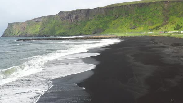 Black sand beach with waves in Vik, Iceland with drone video moving forward.