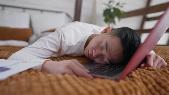 Exhausted Asian Man Sleeping on Laptop Keyboard in Home Office