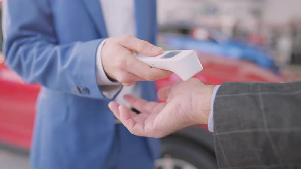 Unrecognizable Car Dealer Measuring Temperature of Client in Dealership with Contactless Thermometer