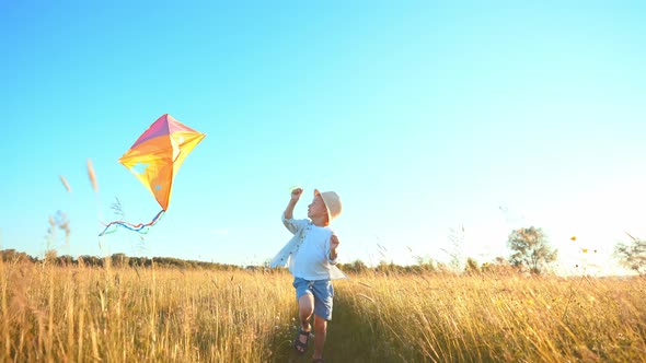 Fast Little Boy Runs Across the Field with a Kite in His Hands Fluttering in Wind Over His Head