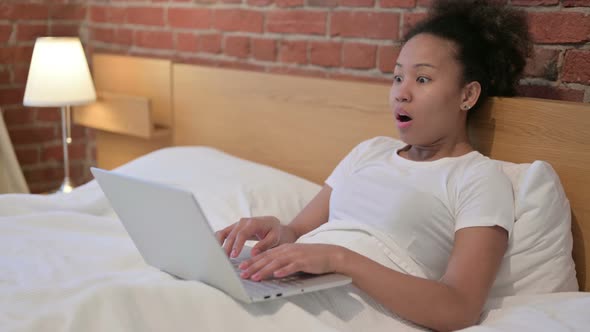 African Woman with Laptop Looking Shocked in Bed