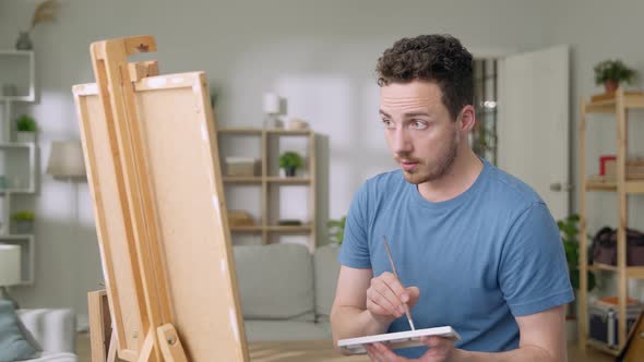 Young Man is Working in His Modern Home Studio in the Morning Drawing on Canvas Enjoying the Process