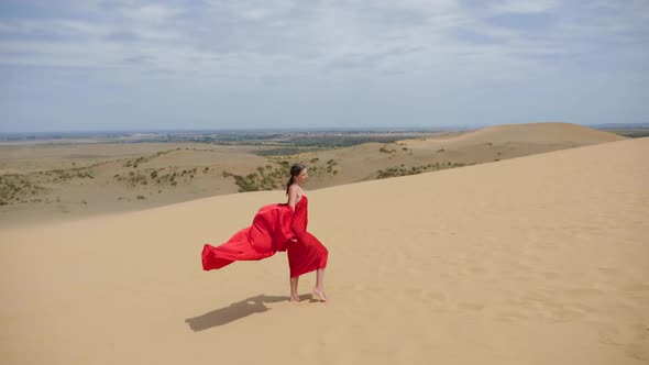 Sexy Brunette Woman in a Red Satin Long Dress Walks on Sand Dunes in the Desert