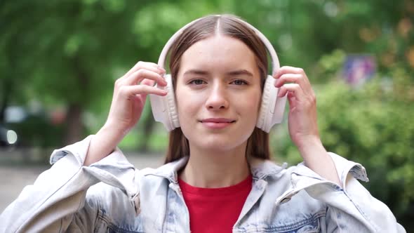 Girl looks straight into the camera and puts on white wireless headphones