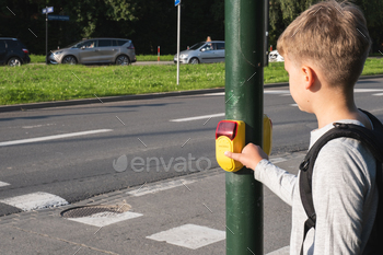 Schoolboy near pedestrian crossing and presses yellow device with button on demand on traffic light