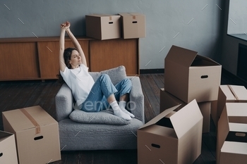 er packing cardboard boxes for moving in new apartment. Hispanic girl stretching arms, dreaming about future home interior. Relocation, first realty.