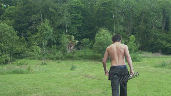Wide shot Topless man walking up field with rake