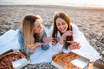 Cheerful young adult girls eating pizza at beach over sea. Vacation season