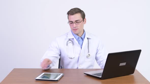 Young Handsome Man Doctor Using Digital Tablet and Laptop Against Wooden Table