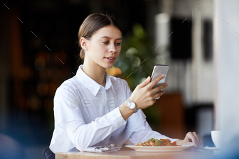 g at table with dish and checking messenger on smartphone while having business lunch in restaurant