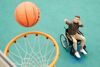  in wheelchair and biting lip while throwing ball in basket on sports ground