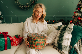 A woman in pajamas opens Christmas gifts.