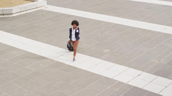 African american businesswoman talking on smartphone and walking with luggage