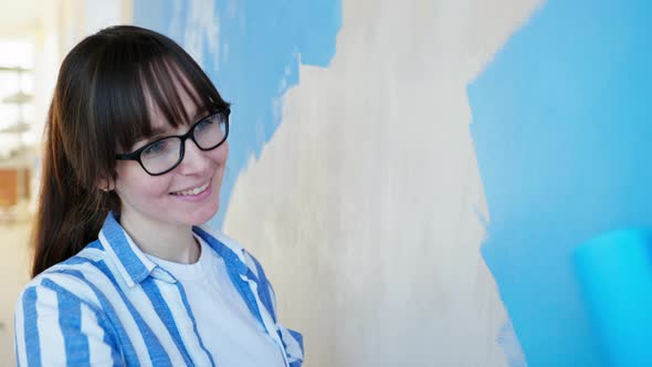 Female House Painter with Construction Roller in Hands Paints Walls with Blue Paint During an Indoor