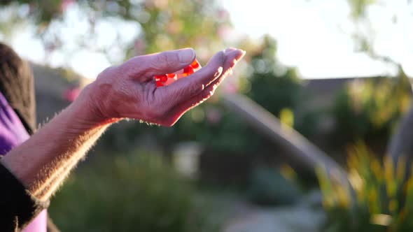 The hands of an old woman tossing a bunch of prescription drug pills into the air in slow motion.