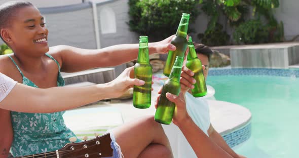 Group of happy diverse male and female friends toasting with beer at pool party