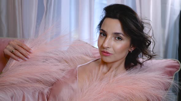 Romantic Woman in Pink Clothes is Lying on the Sofa with Pink Feather