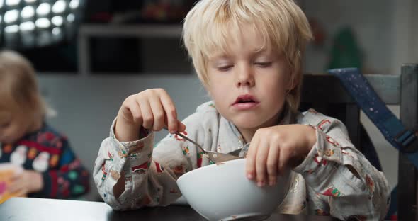 Child Boy Eats Porridge Using Spoon in Dinning Room After School and Speaking