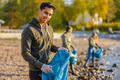 Man collects garbage in bag with group of volunteers on sunny day - PhotoDune Item for Sale