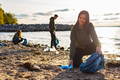 Smiling young woman cleaning beach with a team of volunteers during sunset - PhotoDune Item for Sale