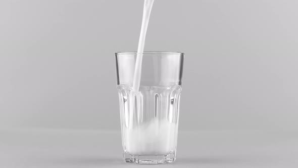 Milk Pouring Into Faceted Glass Close Up Isolated on Light Grey Background