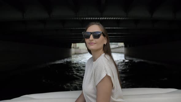 Young Woman Sits in Motorboat Sailing Under Large Bridge