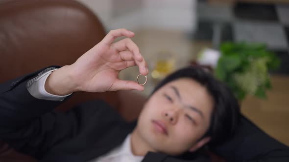 Closeup of Wedding Ring in Male Hand with Blurred Face of Asian Groom at Background