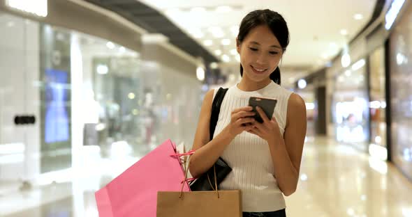 Woman using cellphone and holding shopping bags in shopping center