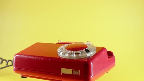 Close Up Hand Picks Up Red Landline Phone on Yellow Background