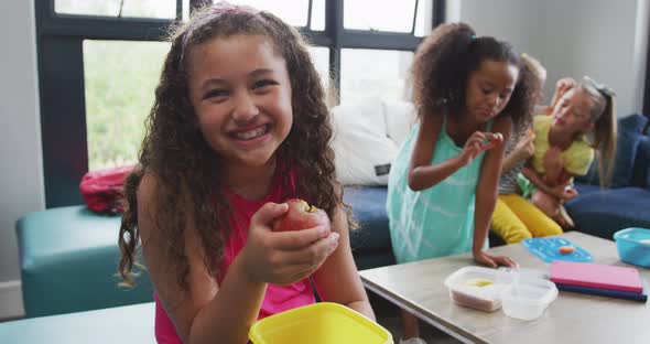 Video of happy biracial girl sitting with friends at school common room and eating