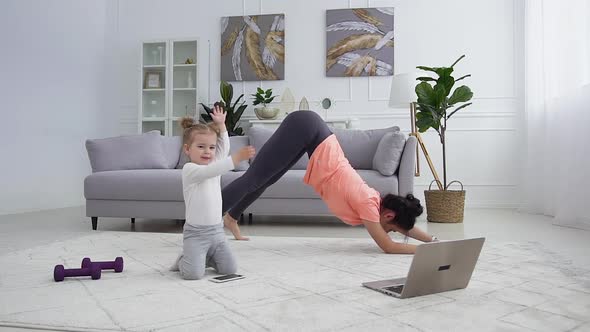  Woman Doing Cat Yoga Pose while Her Smiling Small Daughter Watching Funny Cartoon on Phone